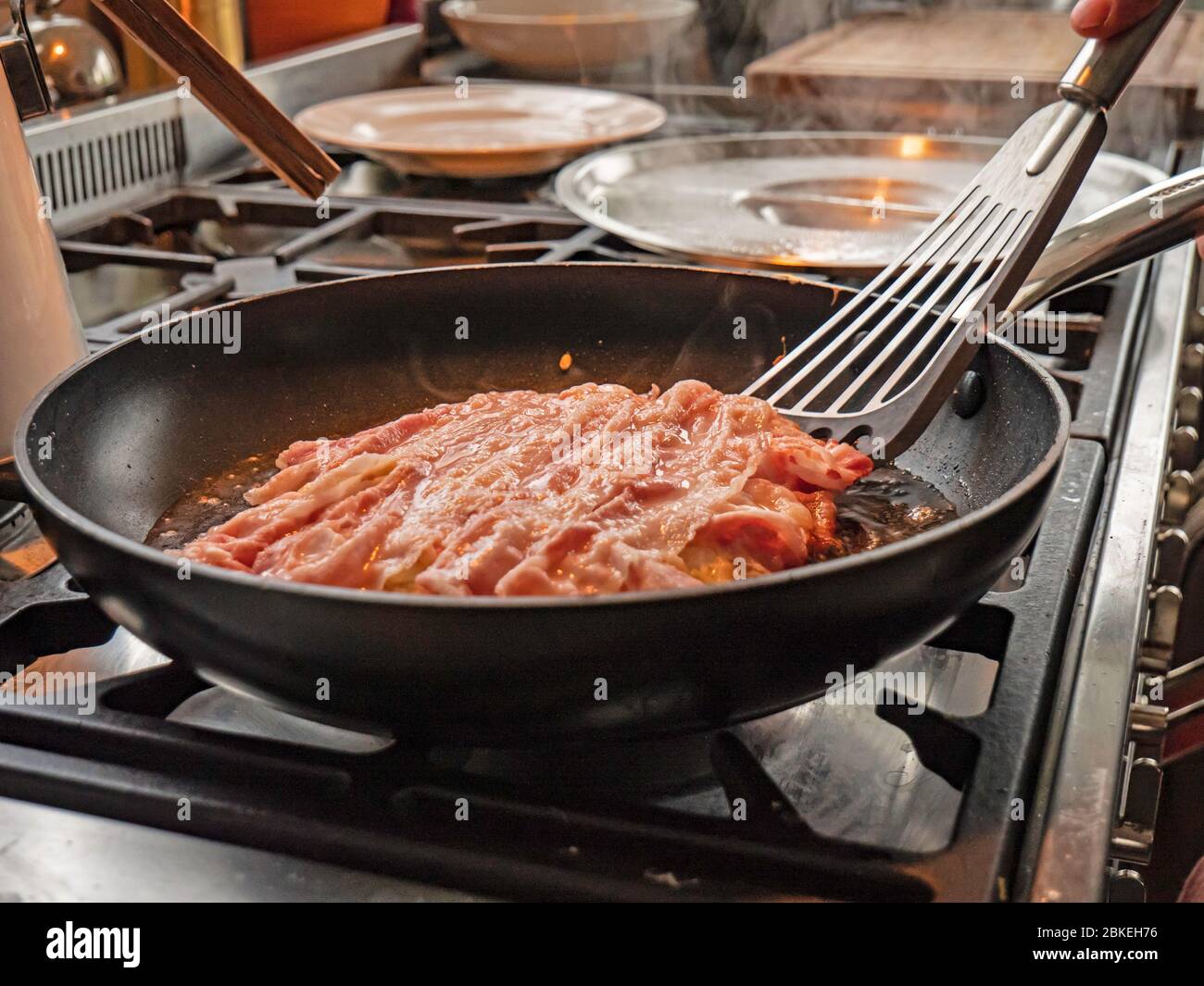 Un chef cuisinra des crêpes okonomiyaki traditionnelles dans une huile chaude dans une casserole. Le mélange de crêpes japonaises est retourné pour voir le dessous doré. Banque D'Images