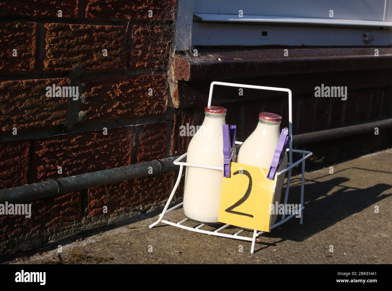 Caisse de lait sur l'allée à côté de la porte d'entrée d'une maison avec livraison de lait à deux pas, deux pintes de lait demi-écrémé en bouteilles de verre réutilisables. Banque D'Images