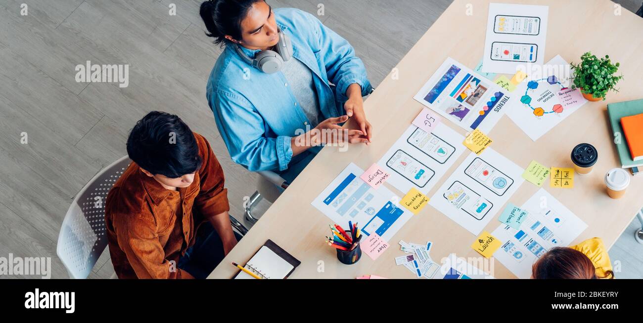 Vue du haut développeur et concepteur d'interface utilisateur d'ux asiatique remue-méninges sur la conception d'éléments filaires d'interface d'application mobile sur table avec le code de couleur et le code de Breif du client à M. Banque D'Images