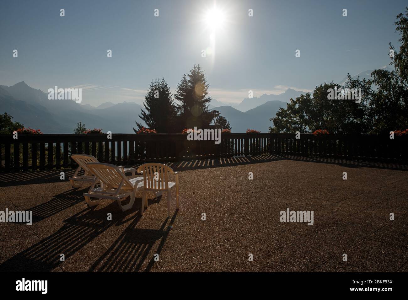 Terrasse avec vue sur la montagne, clôture en bois décorée de plantes en pot, chaises en plastique vides, deux chaises longues pour bronzer et ombre en fonte relaxante Banque D'Images