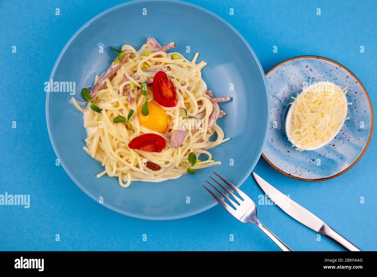 Pâtes Carbonara - spaghetti avec petits morceaux de bacon, mélangés avec une sauce aux œufs et au parmesan. Plaque bleue sur fond bleu. Macanons avec œuf Banque D'Images