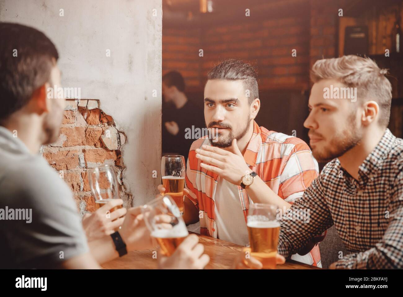 Réunion conviviale. Les gars boivent de la bière au bar. L'homme barbu avec des yeux percés raconte une histoire intéressante, les hommes écoutent. Banque D'Images