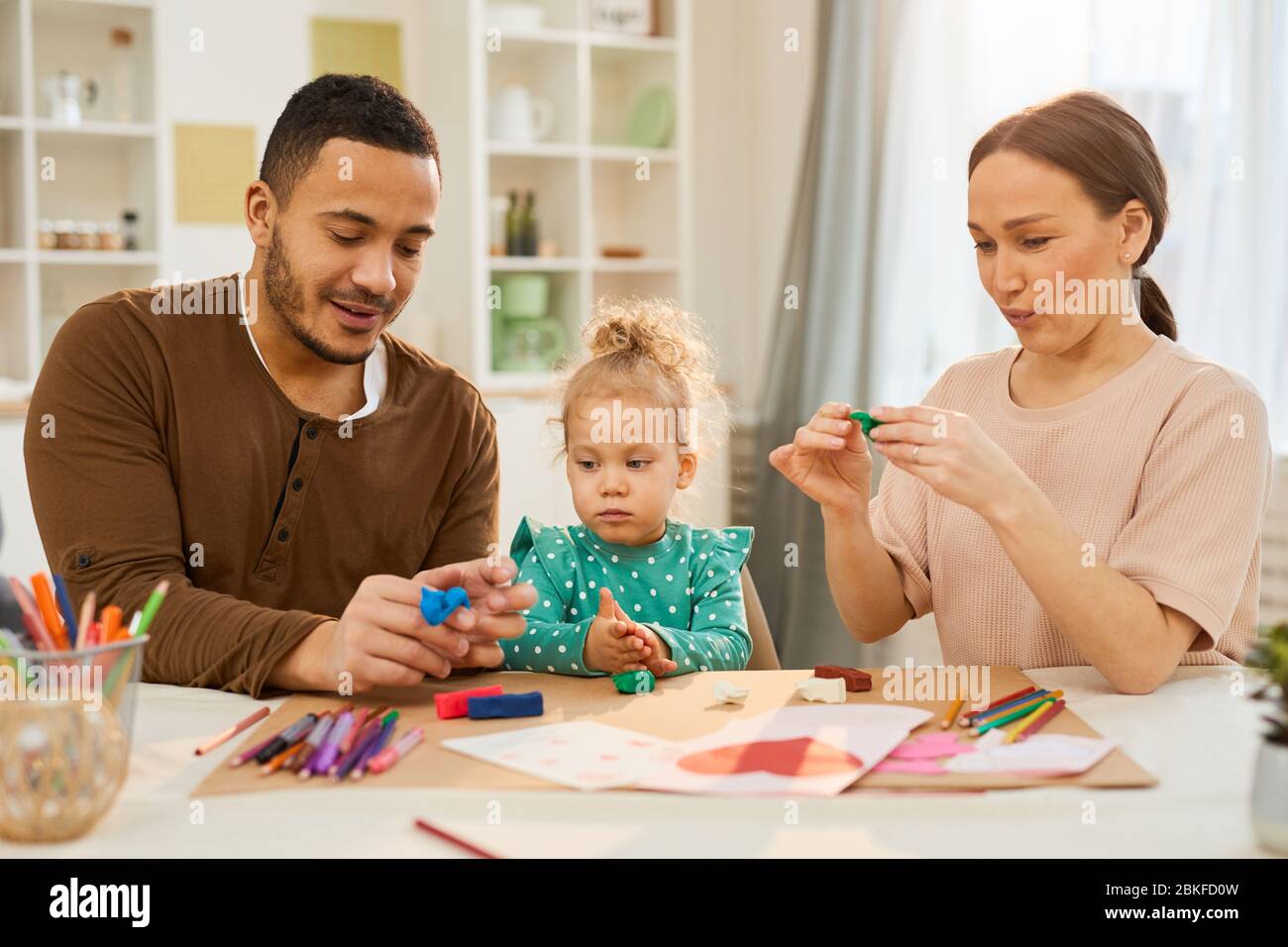 Les parents adorants passent avec leur petite fille assise ensemble à des modèles de fabrication de table utilisant la pâte de jeu Banque D'Images