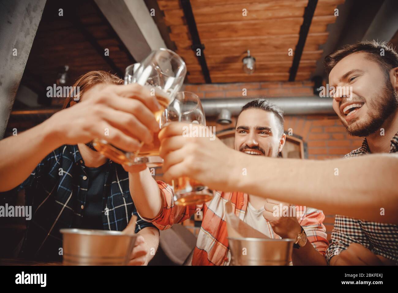Les gars bizarres boivent de la bière au pub. Lunettes à clinking sur le bar de style Texas, fond de mur en briques de bois. Banque D'Images
