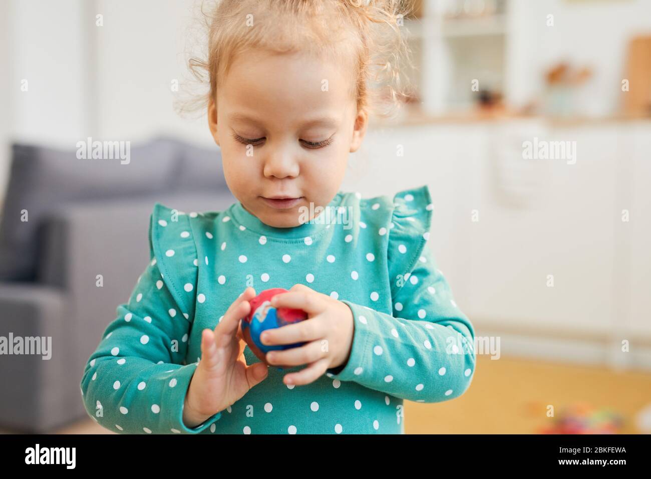 Petite fille caucasienne portant des vêtements à pois turquoise, faisant une boule d'argile à modeler colorée, portrait horizontal tourné Banque D'Images