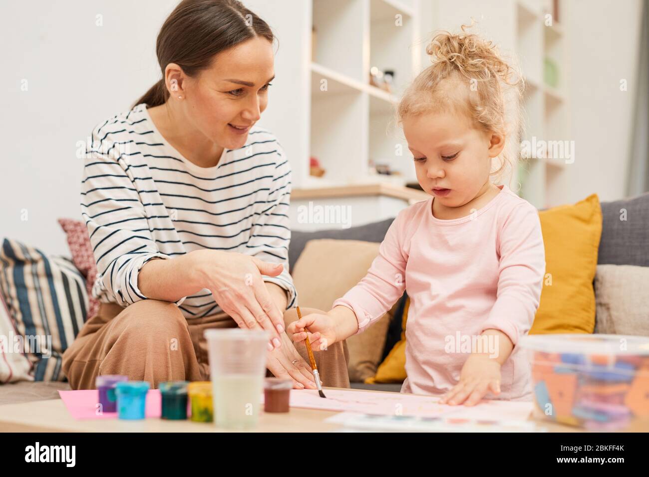 Jeune femme passe du temps avec sa fille à la maison lui enseignant pour peindre des images, photo horizontale Banque D'Images