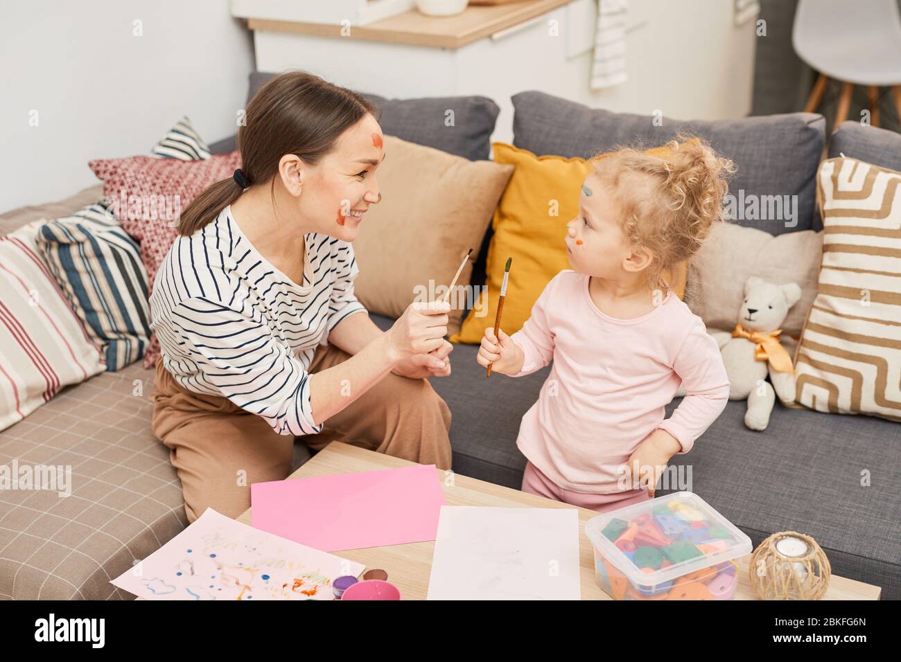 Photo horizontale à angle élevé de la jeune femme s'amuser avec sa petite fille peindre des taches colorées sur leurs visages Banque D'Images