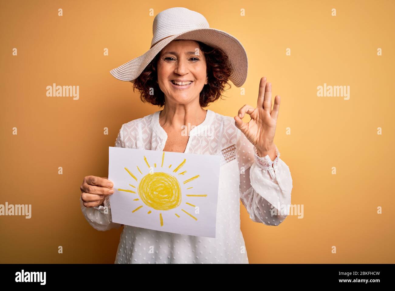 Femme maubrée d'âge moyen en vacances à bunner avec image du soleil sur fond jaune faisant bon signe avec les doigts, excellent symbole Banque D'Images