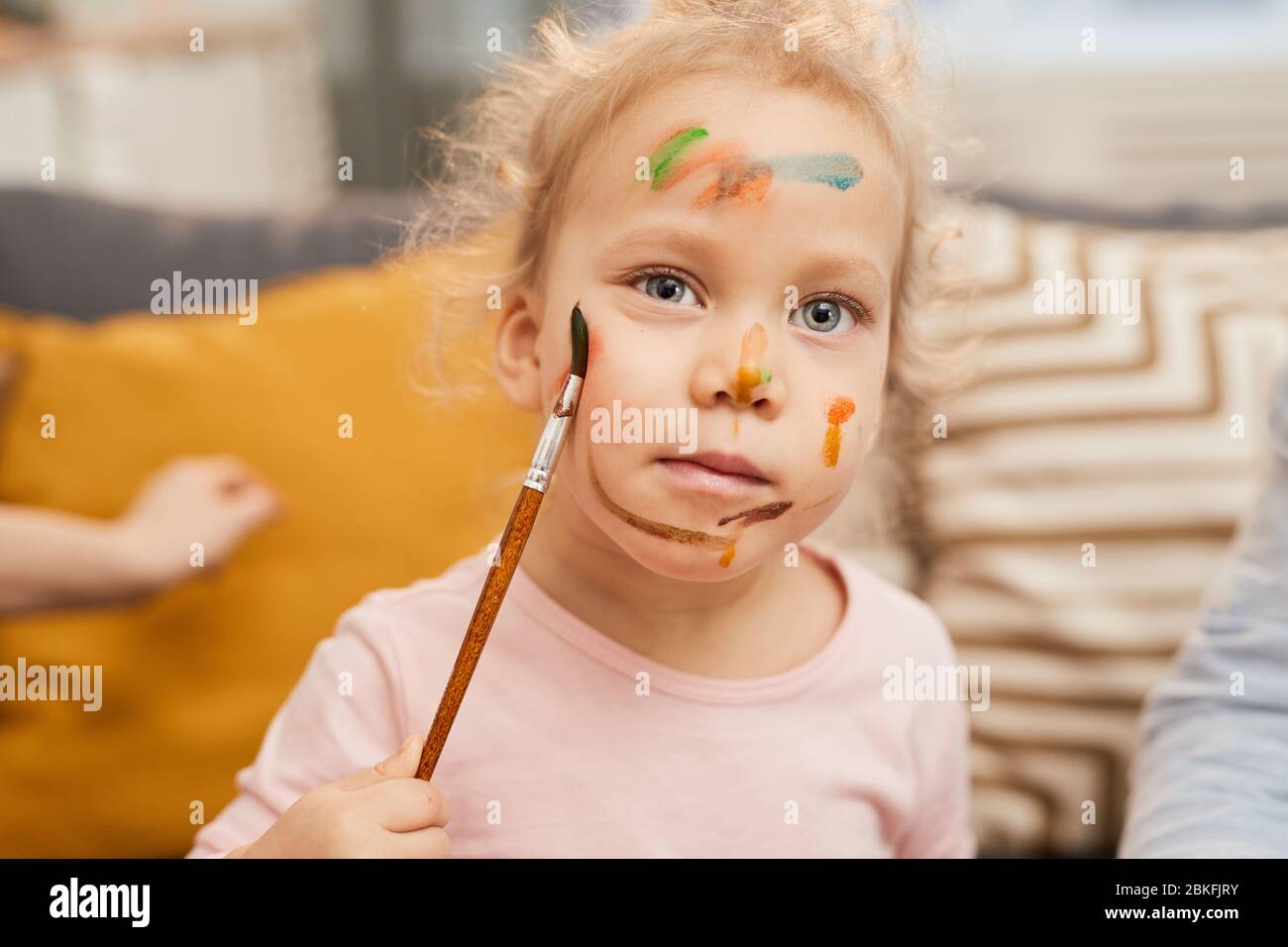 Portrait de taille moyenne de petite fille caucasienne peignant des coups de gouache sur son propre visage Banque D'Images