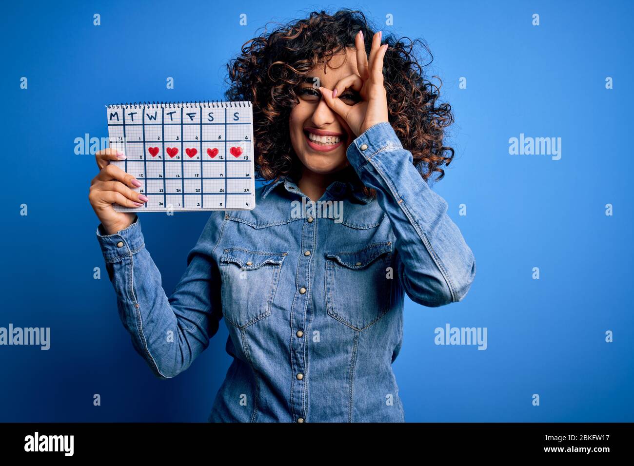 Jeune femme arabe curieuse tenant calendrier de période contrôlant le cycle  menstruel avec un visage heureux souriant faisant bon signe avec la main  sur les yeux regardant th Photo Stock - Alamy