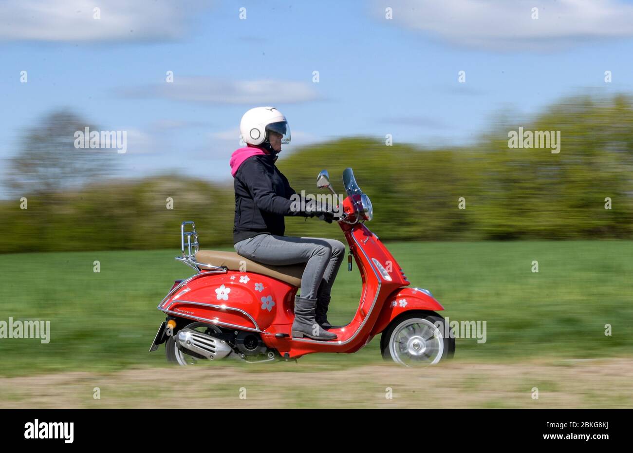 Kiel, Allemagne. 04 mai 2020. Par temps ensoleillé, une femme conduit son scooter  Vespa 125 cc rouge le long d'une route de terre portant des vêtements de  sécurité, un casque et des