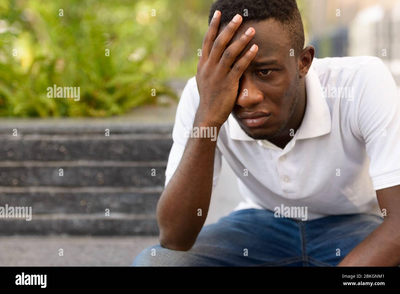Portrait de jeune homme africain stressé regardant déprimé en s'assoir à l'extérieur Banque D'Images