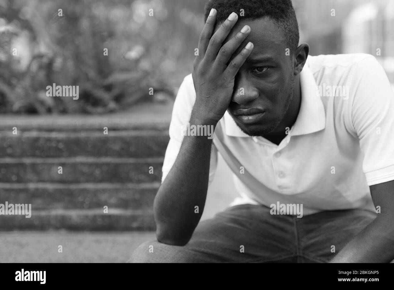 Portrait de jeune homme africain stressé regardant déprimé en s'assoir à l'extérieur Banque D'Images
