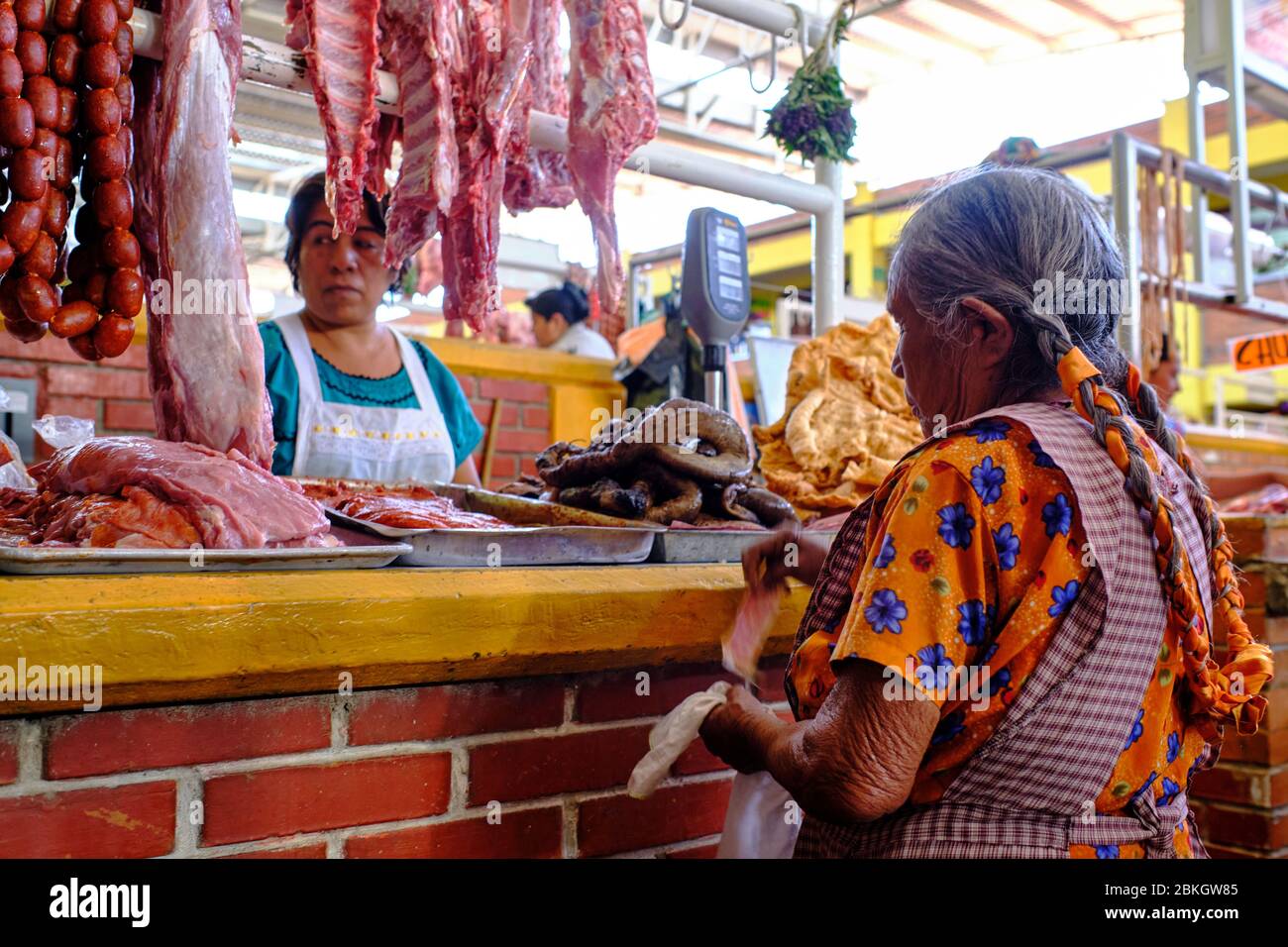 Vieille dame autochtone avec des tresses payant avec de l'argent pour la viande qu'elle a achetée dans un boucher dans le marché de Zaachila. Banque D'Images