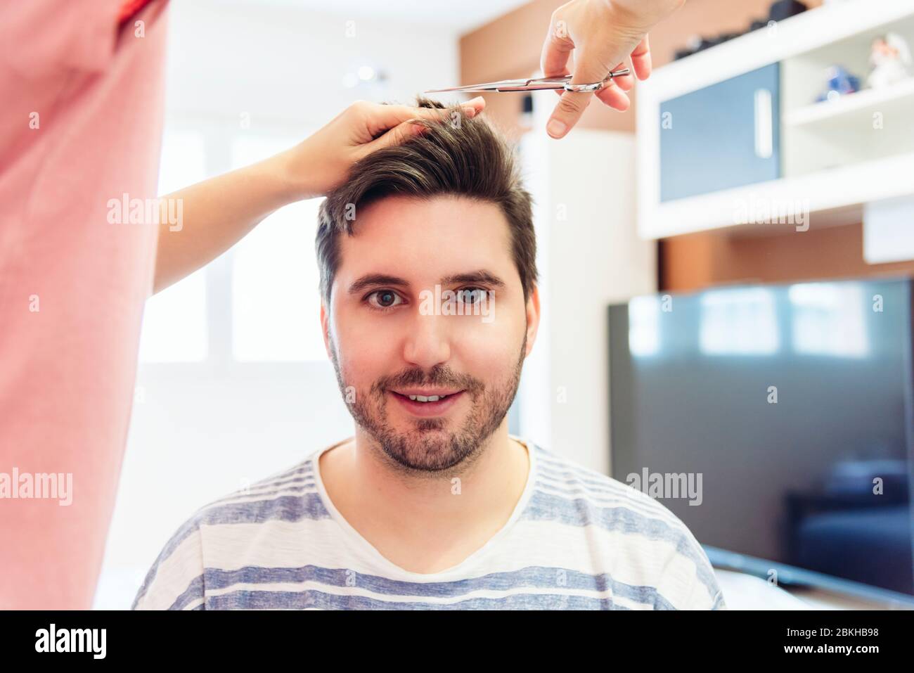 Femme coupant les cheveux d'un jeune homme dans un coiffeur de fortune à la maison. Concept de quarantaine. Banque D'Images