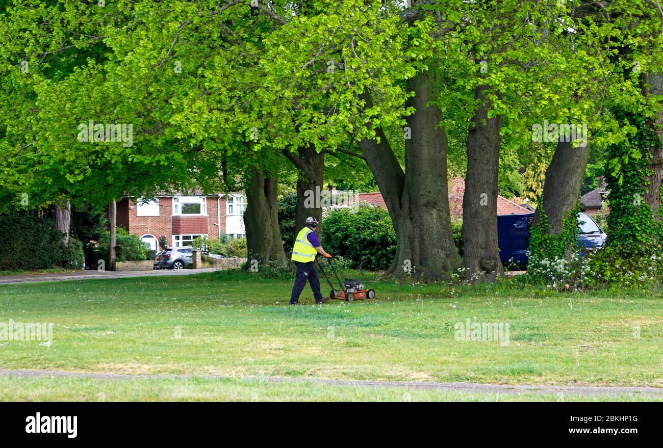 Un homme s'est engagé dans la coupe d'herbe sur un petit vert dans une zone résidentielle de Hellesdon, Norfolk, Angleterre, Royaume-Uni. Banque D'Images