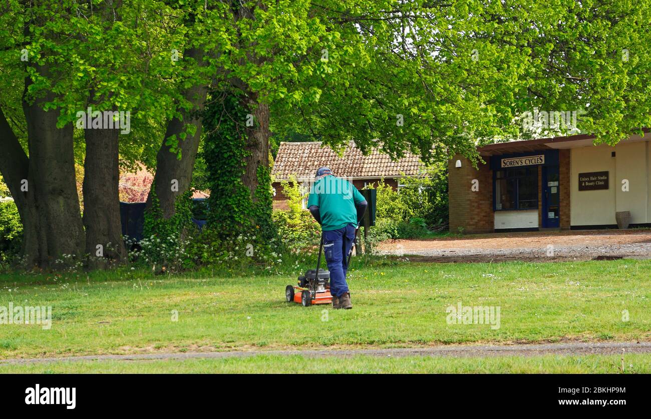Un homme s'est engagé dans la coupe d'herbe sur un petit vert dans une zone résidentielle de Hellesdon, Norfolk, Angleterre, Royaume-Uni. Banque D'Images