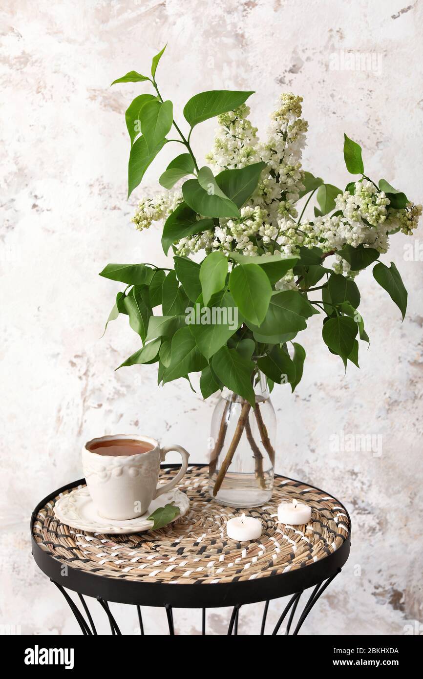 Vase avec de belles fleurs lilas, tasse de thé et bougies sur la table près du mur clair Banque D'Images