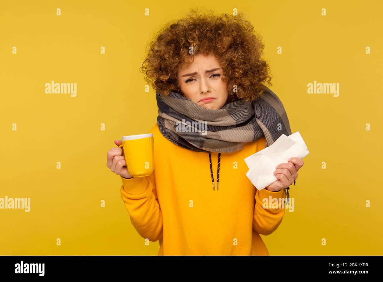 Traitement de la grippe. Femme atteinte de grippe malheureuse et dépressive avec cheveux bouclés, enveloppée dans un foulard chaud, tenant une serviette et du thé chaud, se frognant avec le mal mécontent Banque D'Images