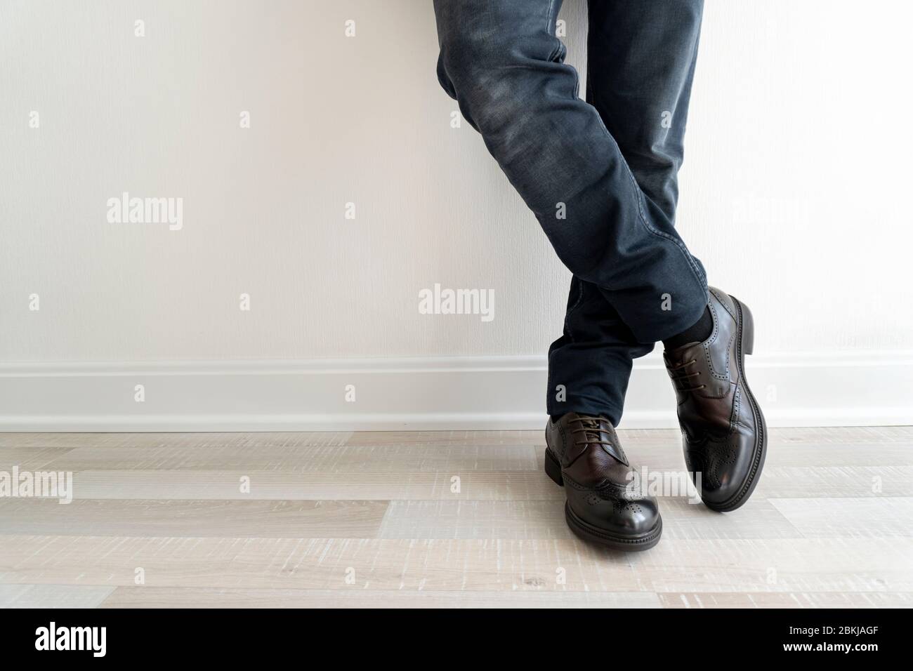 Jeune homme à jeans noirs et montrant ses nouvelles chaussures marron restant près du mur Banque D'Images