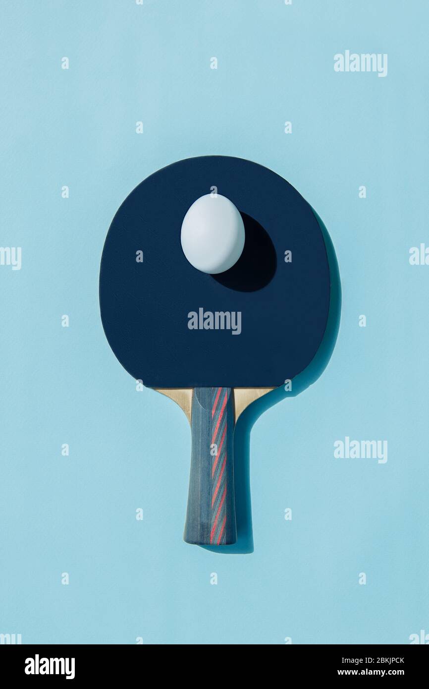 Un œuf blanc repose sur une raquette de ping-pong bleue. Une ombre tombe de l'oeuf. La poignée de la raquette comporte des rayures rouges. Banque D'Images