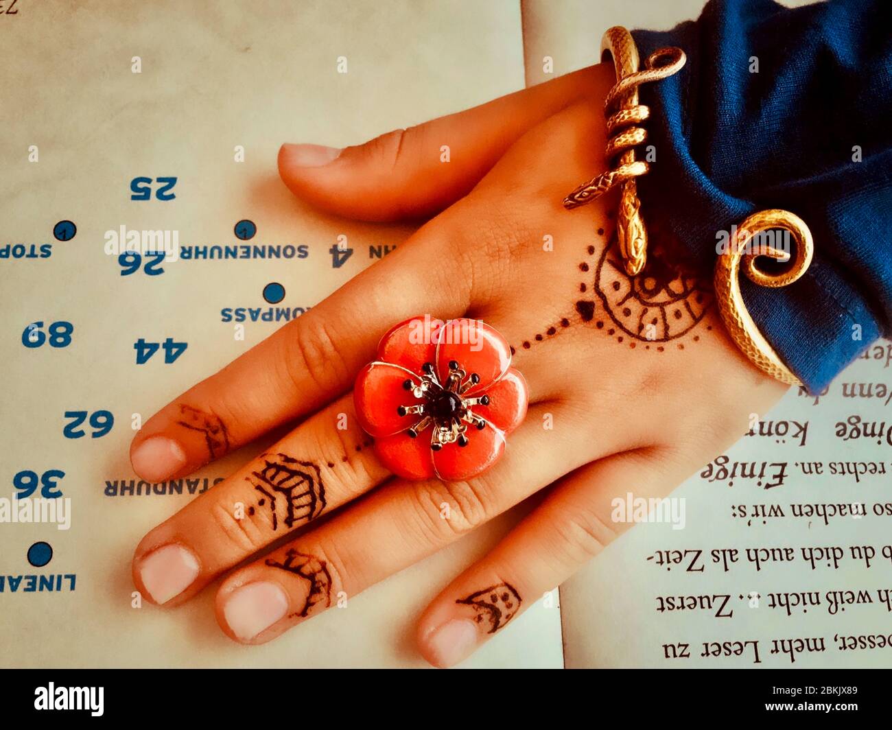 Main d'une fille avec bague et bracelet percutant, ainsi qu'un tatouage au henné couché sur une librairie ouverte Banque D'Images