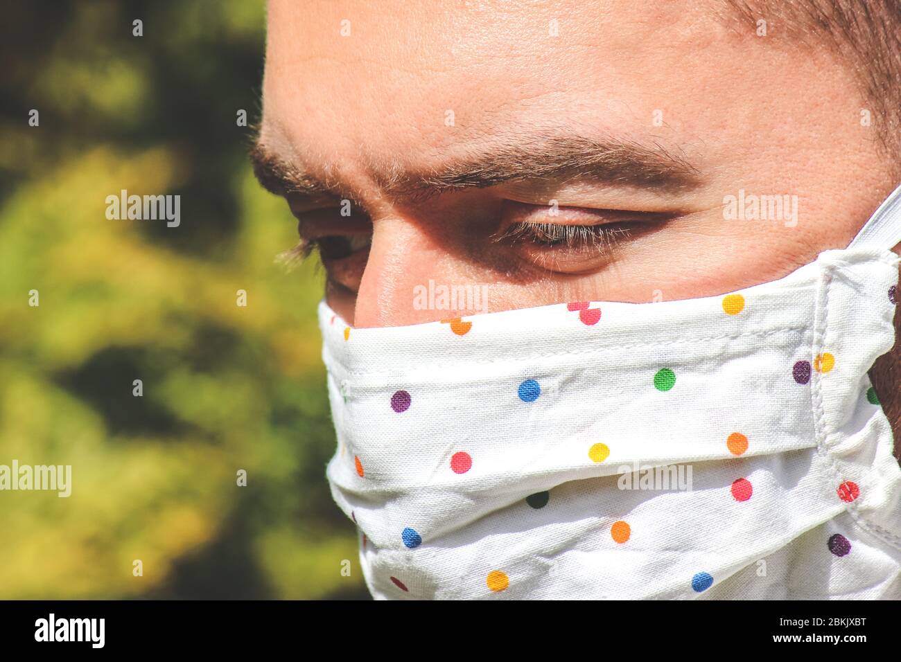 Jeune homme caucasien avec un masque facial fabriqué à la main en tissu pendant une pandémie de coronavirus. Coronavirus, éclosion de COVID-19. Concept de protection contre les virus. Arrière-plan flou. Visage et yeux. Photo horizontale. Banque D'Images