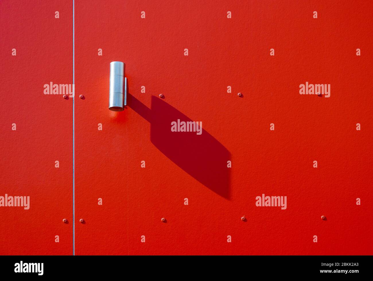 Lampe d'extérieur moderne avec ombre sur un mur rouge lors d'une journée ensoleillée, détail minimaliste architectural Banque D'Images