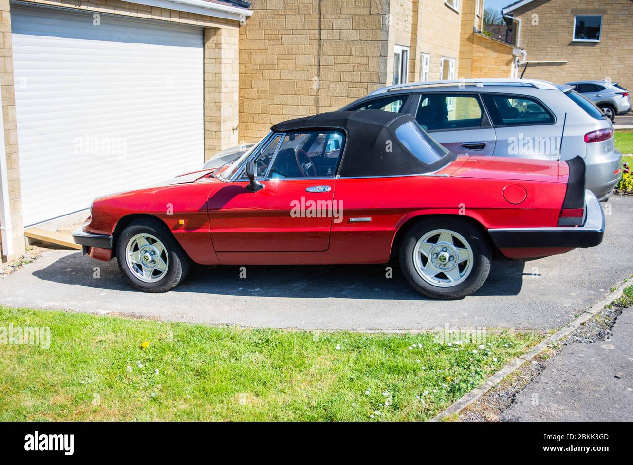 Une araignée rouge Alfa-Romeo, voiture de sport 2 places, garée sur une allée devant une porte de garage Banque D'Images
