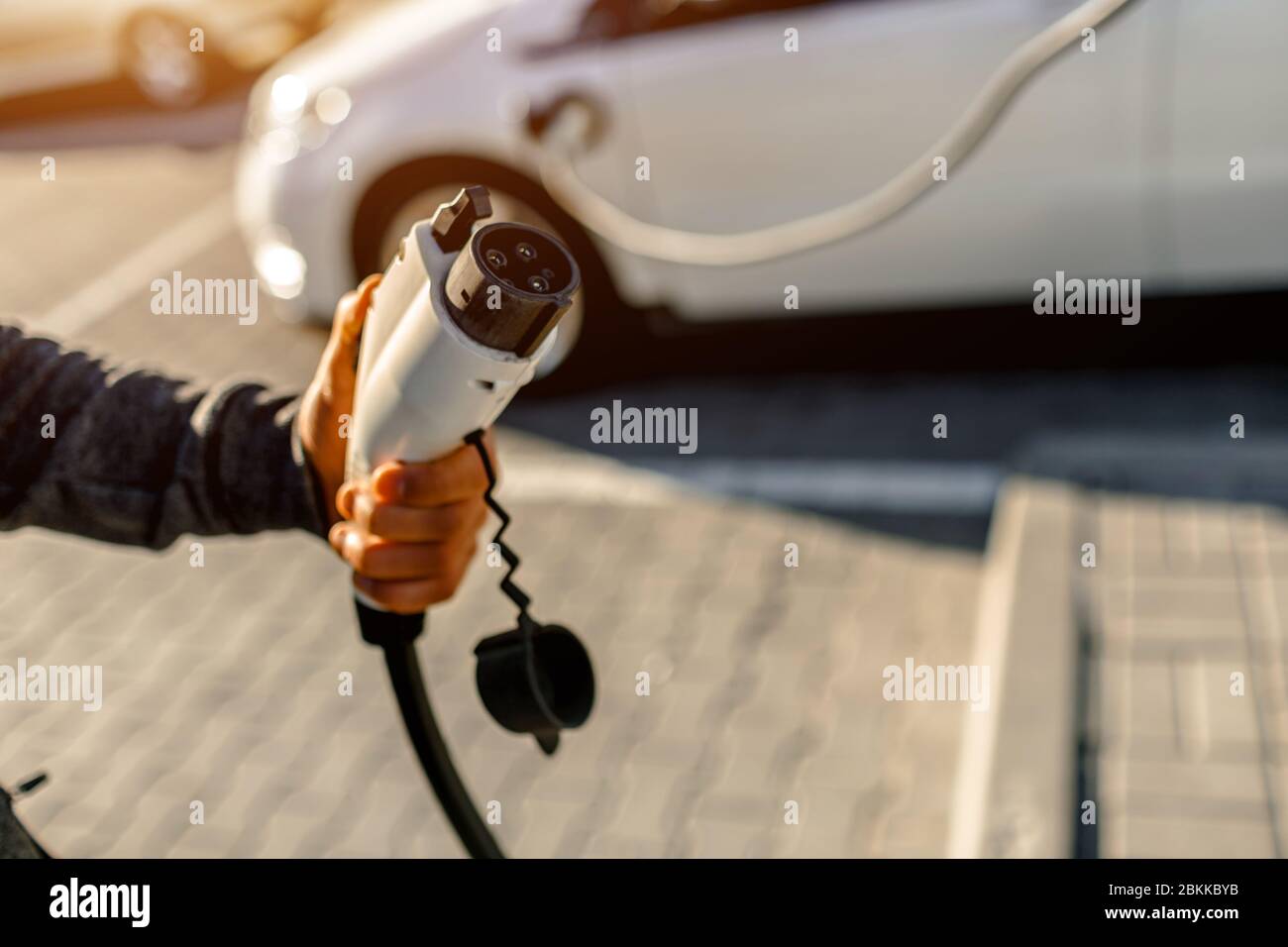 Homme tenant le câble de charge électrique pour voiture électrique dans le parking extérieur . Gros plan Banque D'Images