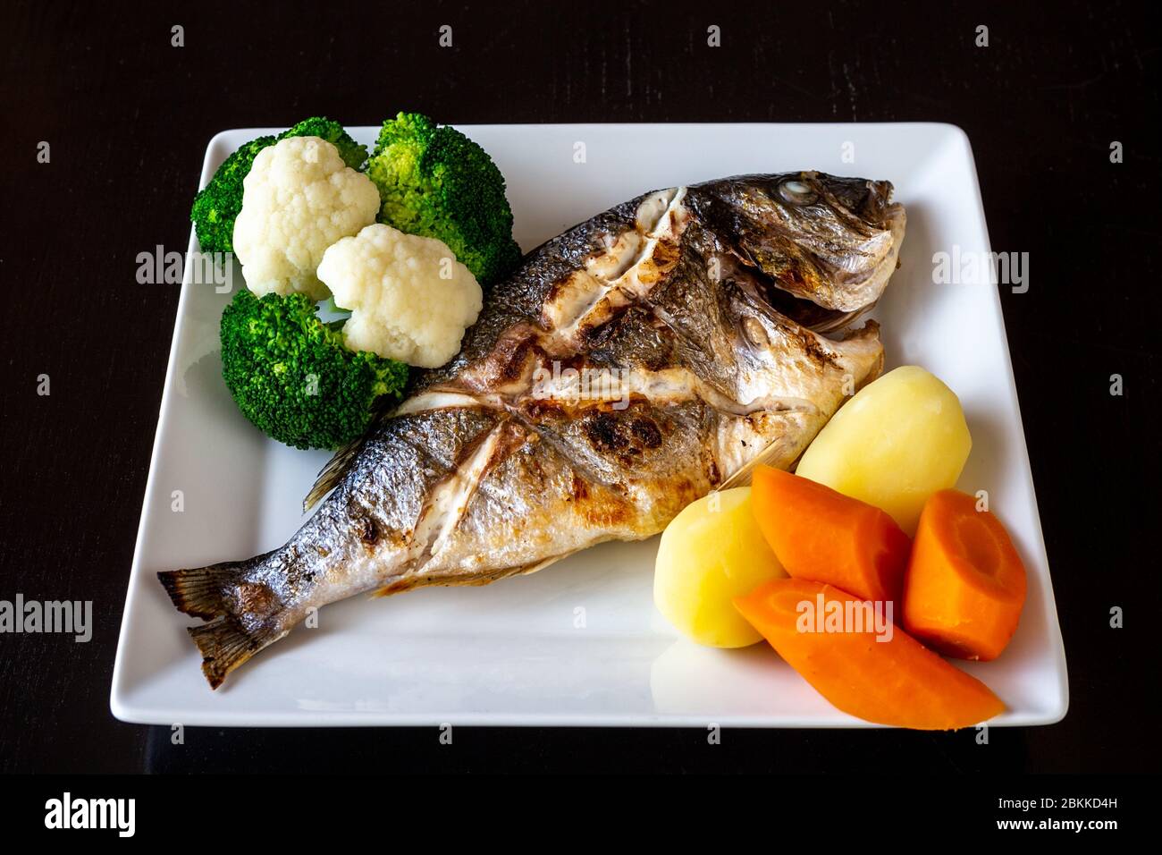 Plat de mer méditerranéen, Sparus aurata de légumes de poisson cuits au four et pommes de terre cuites sur fond noir. Une alimentation saine. Banque D'Images