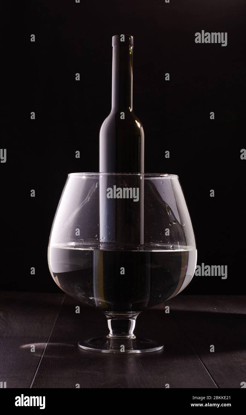 Bouteille de vin en verre foncé dans un immense verre de vin isolé sur fond  noir Photo Stock - Alamy