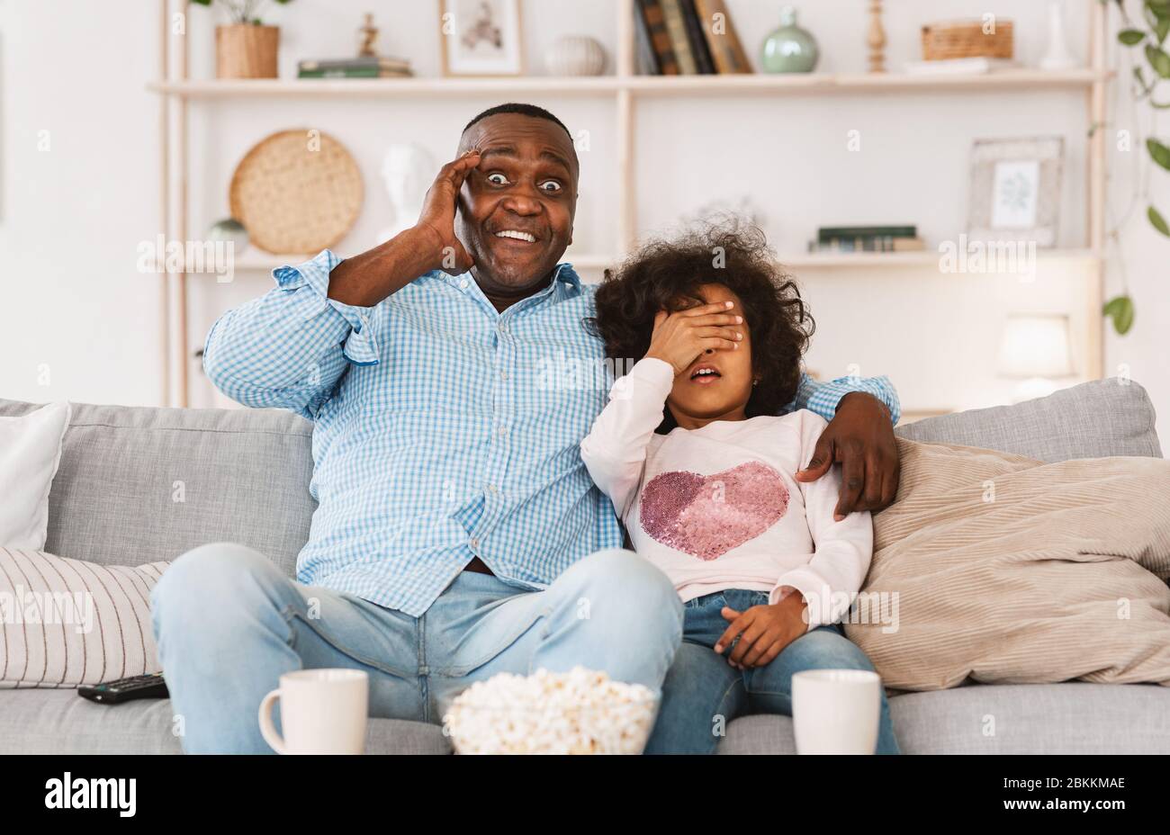 Verrouillez les divertissements familiaux. Un homme afro-américain choqué et une petite-fille effrayée regardant un film effrayant chez soi Banque D'Images