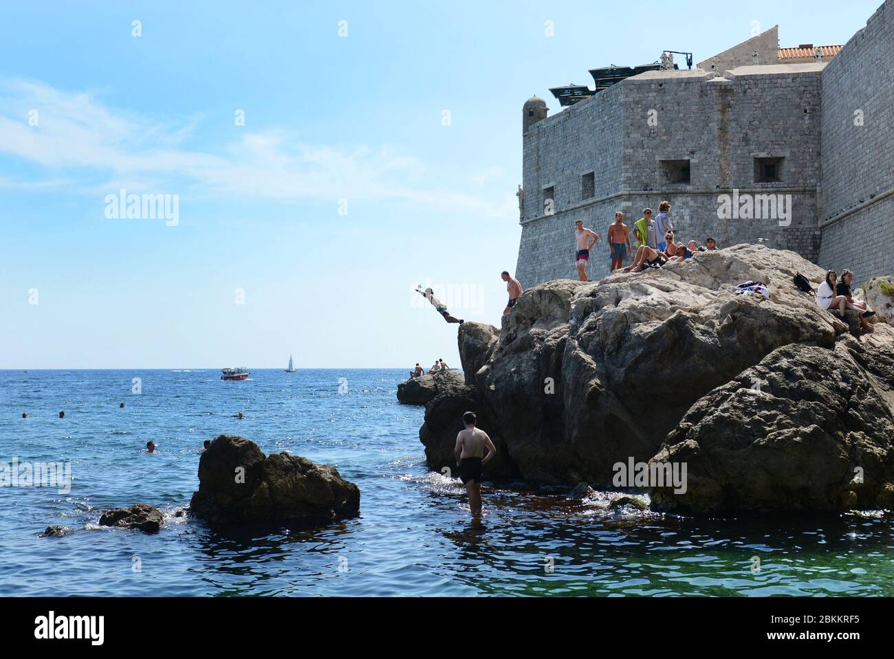 Un homme qui saute dans la mer depuis les falaises près des murs de la vieille ville de Dubrovnik, Croatie. Banque D'Images