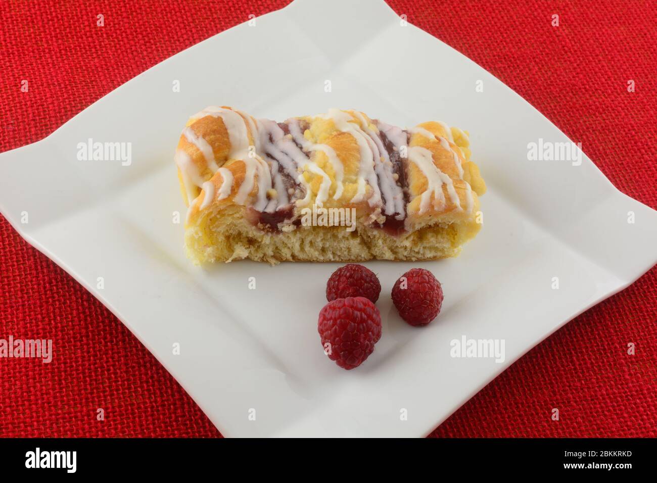 Tranche de gâteau au café framboise avec framboises fraîches sur une assiette blanche sur une nappe rouge Banque D'Images