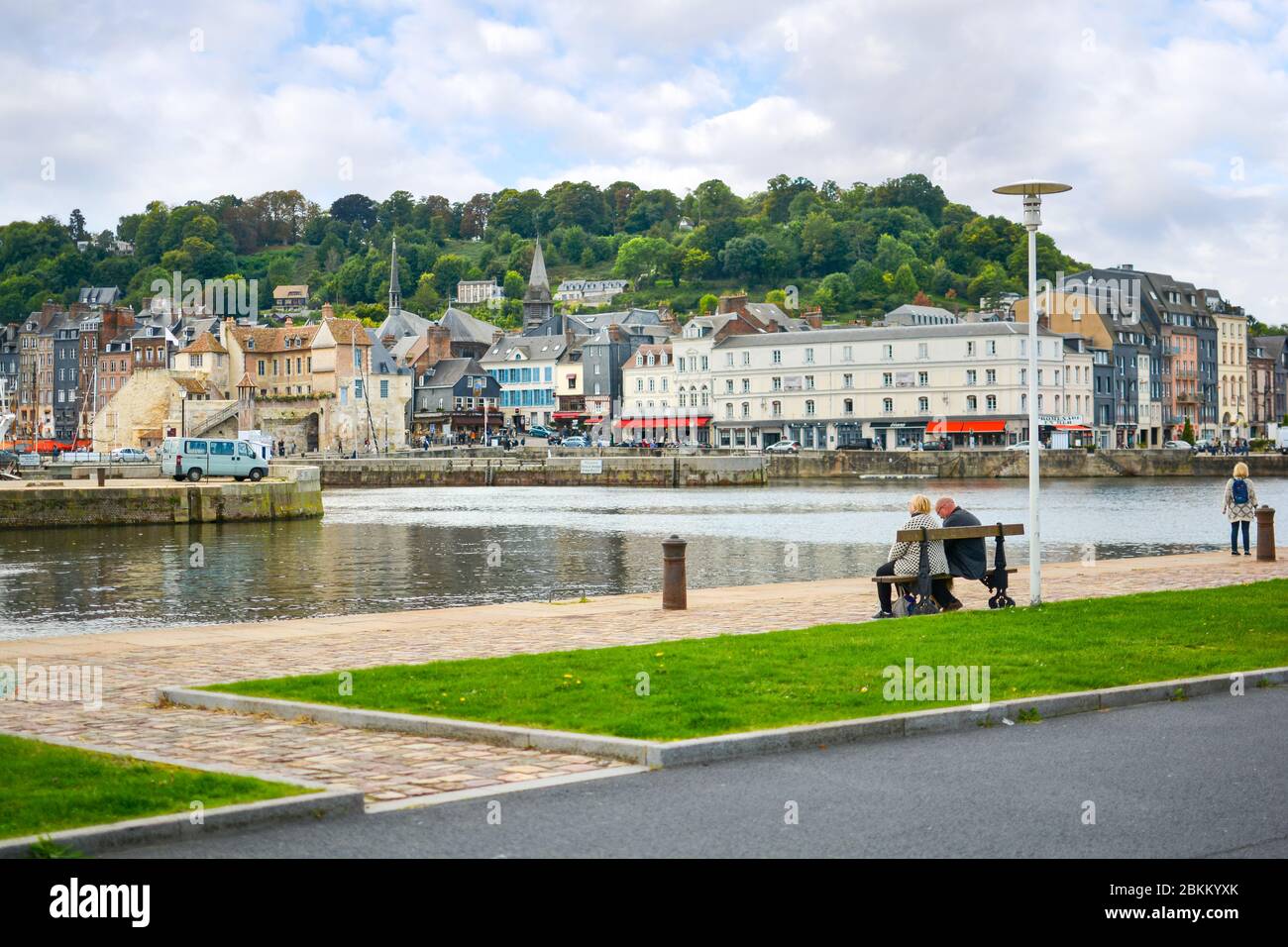 Un vieux couple retraité s'assoit sur un banc de parc et bénéficie de la vue sur le village de pêcheurs de Honfleur France, en Normandie, dans un après-midi partiellement nuageux Banque D'Images