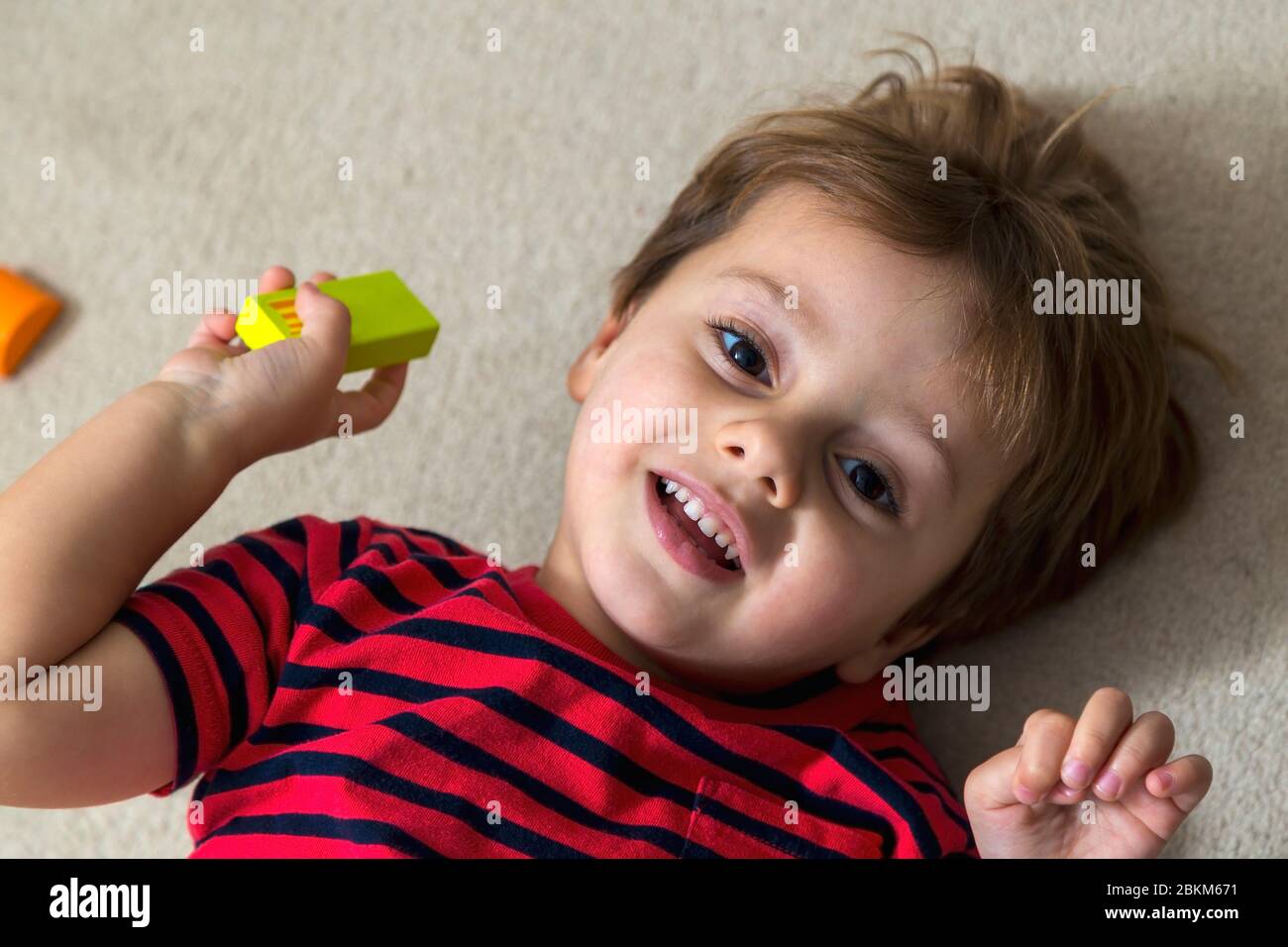 Un petit enfant gai allongé sur la moquette. Portrait d'un garçon de 3 ans jouant sur le sol. Banque D'Images