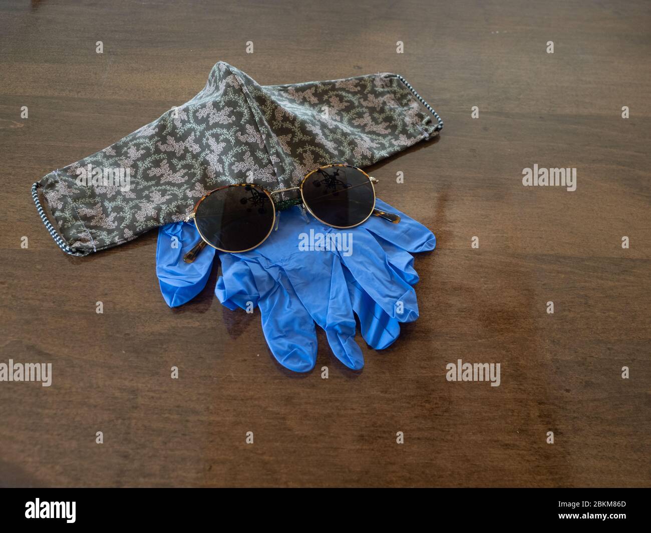 Équipement de protection individuelle avec une paire de gants jetables bleus et un masque en tissu fait main avec lunettes de soleil sur une table en bois. Photographié wi Banque D'Images