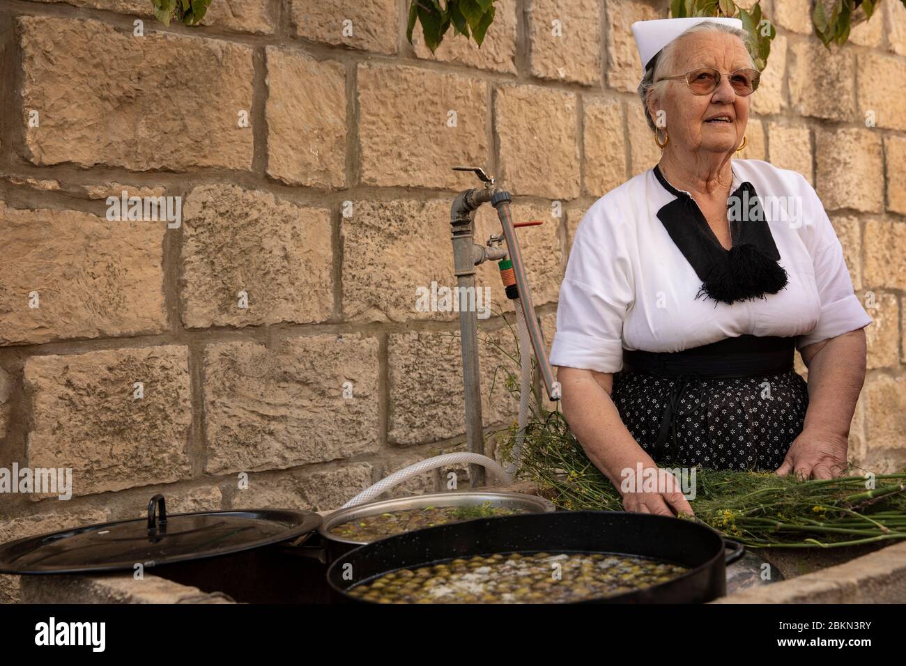 Konavle, Croatie, 5 septembre 2019. Une femme âgée portant un costume traditionnel traditionnel et confectionnés des olives croates typiques avec du sel et un Banque D'Images