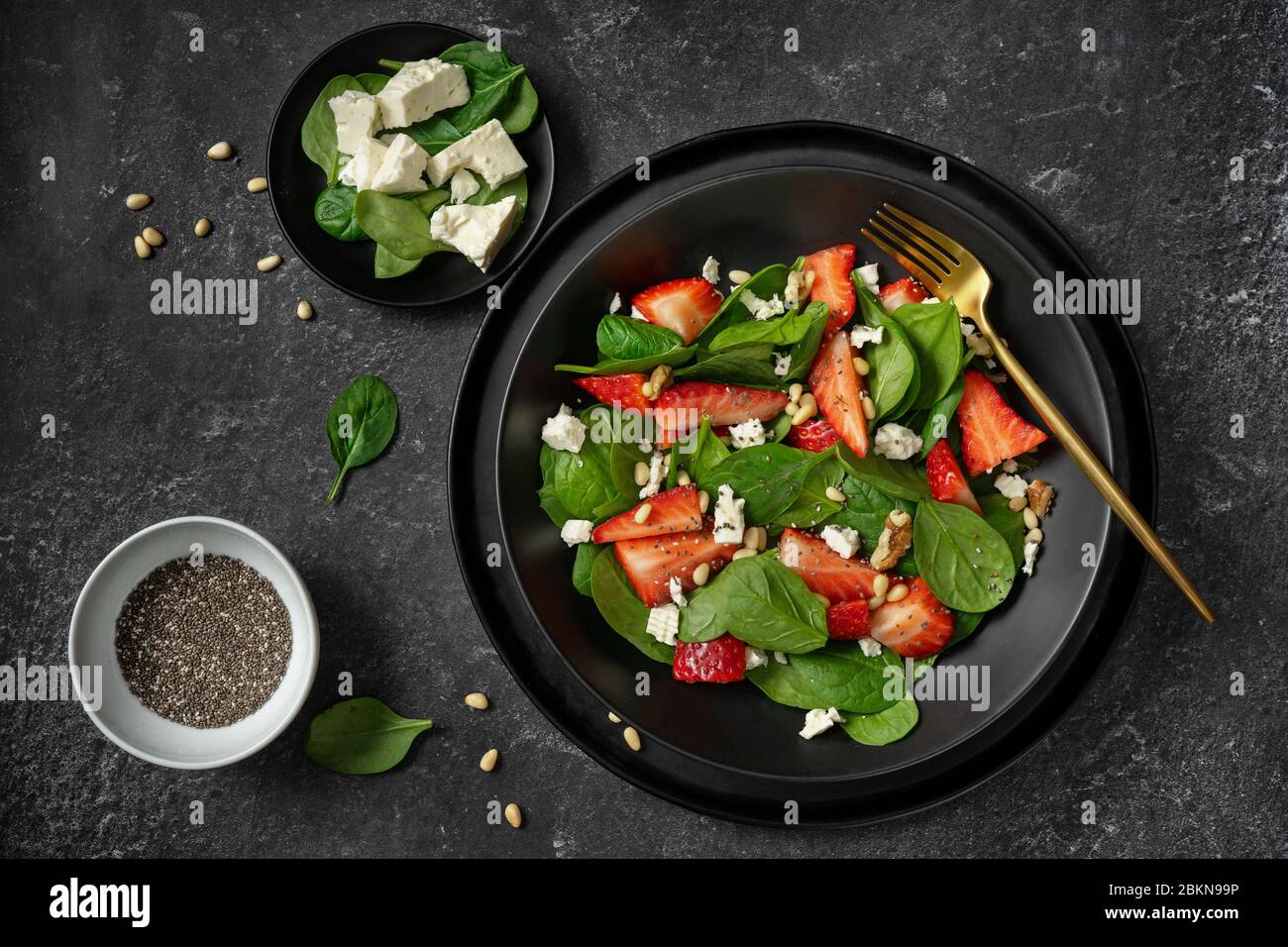 Vue de dessus d'une assiette noire avec salade d'épinards et de fraises et ses ingrédients Banque D'Images