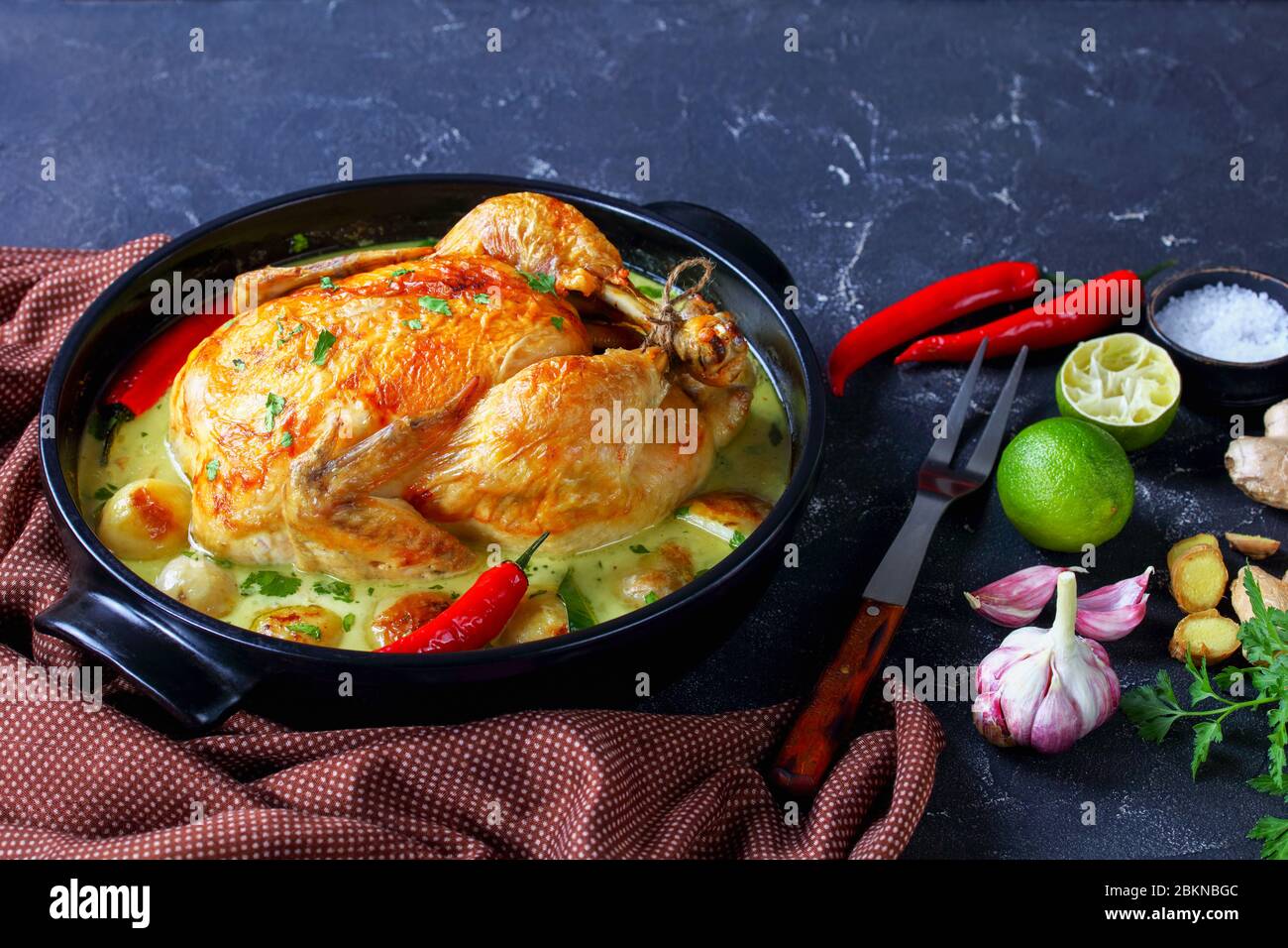 Lait de coco thaïlandais poulet braisé et pommes de terre pour bébés au Chili, feuilles de citron vert kaffir dans un braiser noir sur une table de cuisine avec fourchette à viande et ingrédient Banque D'Images