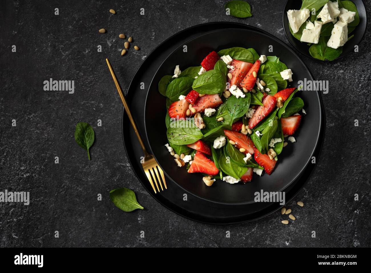 Vue de dessus d'une assiette noire avec une salade d'épinards à la fraise saine Banque D'Images