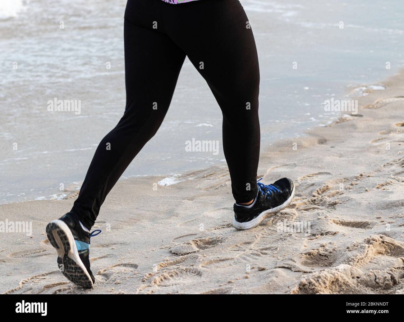 Jambes d'un coureur courant à la plage en spandex noir au bord de l'eau sur le sable. Banque D'Images