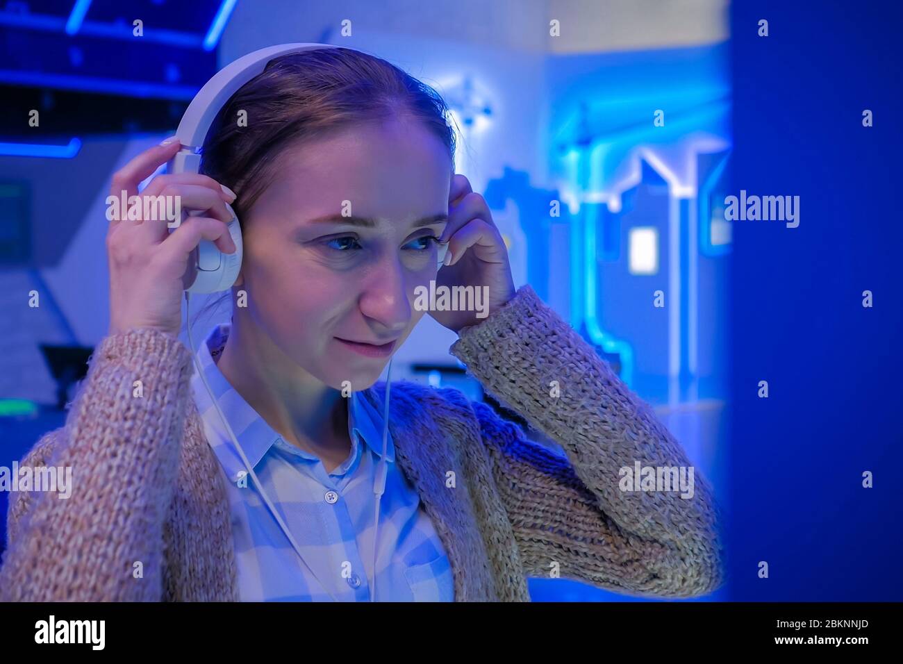 Femme regardant l'exposition, utilisant des écouteurs blancs et écoutant un guide audio dans une exposition futuriste moderne ou un musée. Science-fiction Banque D'Images