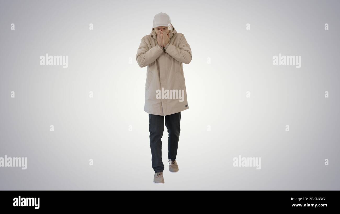 Homme en tenue d'hiver marchant et toussant sur fond dégradé. Banque D'Images