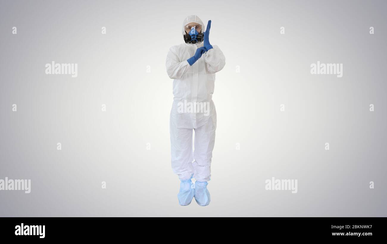 Homme portant des vêtements de protection HAZMAT montrant qu'il porte des gants sur fond dégradé. Banque D'Images