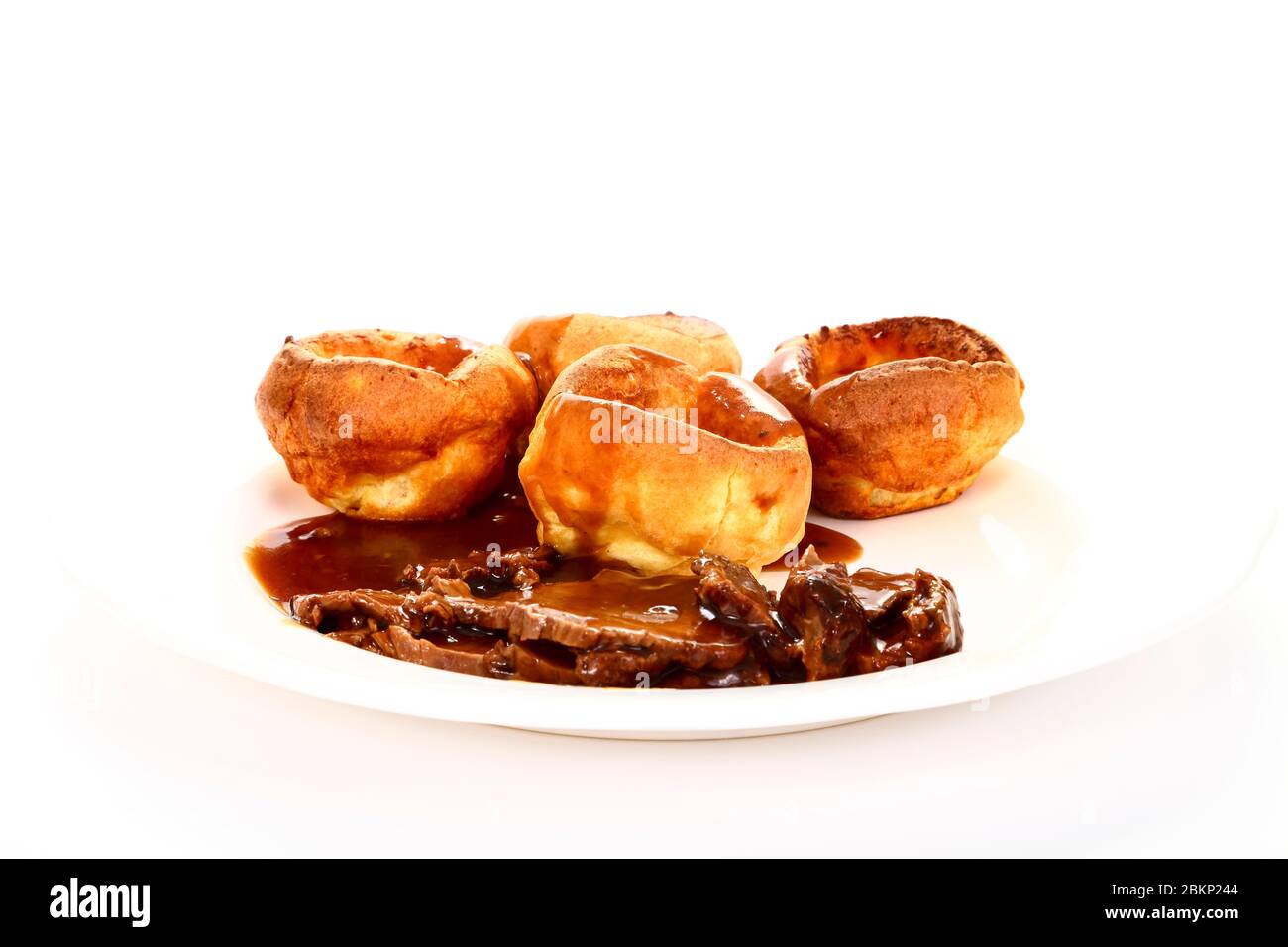 Repas britannique traditionnel de rôti de bœuf et de Yorkshire puddings avec sauce sur une assiette blanche Banque D'Images