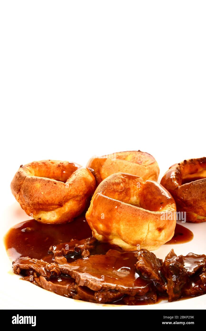 Repas britannique traditionnel de rôti de bœuf et de Yorkshire puddings avec sauce sur une assiette blanche Banque D'Images