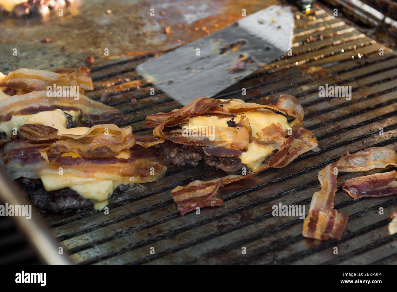 Chef préparant de délicieux hamburgers au fromage avec du bacon et les retournant sur le gril. Banque D'Images