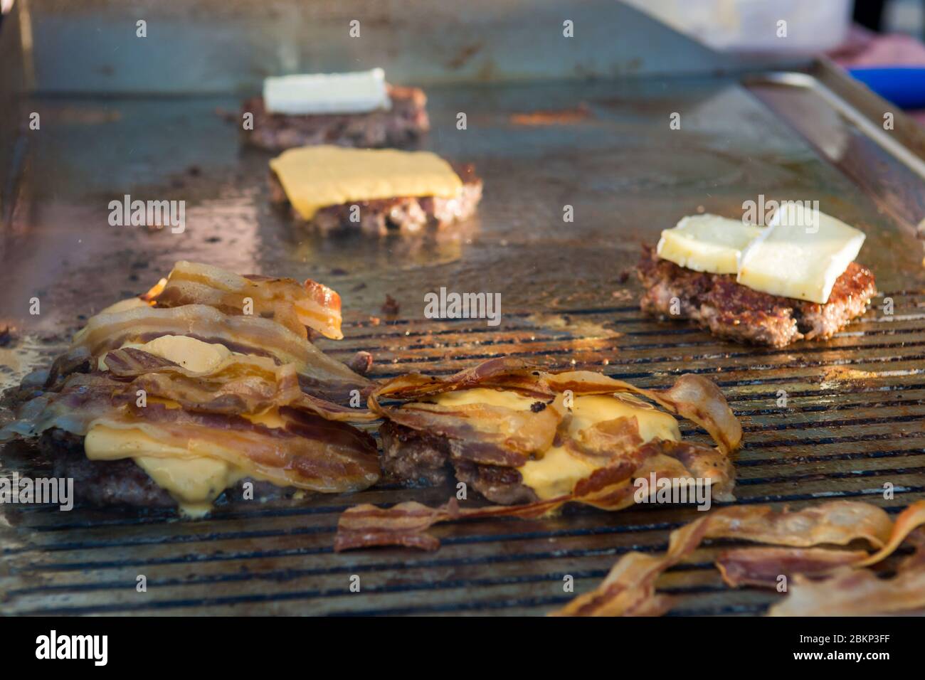 Chef préparant de délicieux hamburgers au fromage avec du bacon et les retournant sur le gril. Banque D'Images